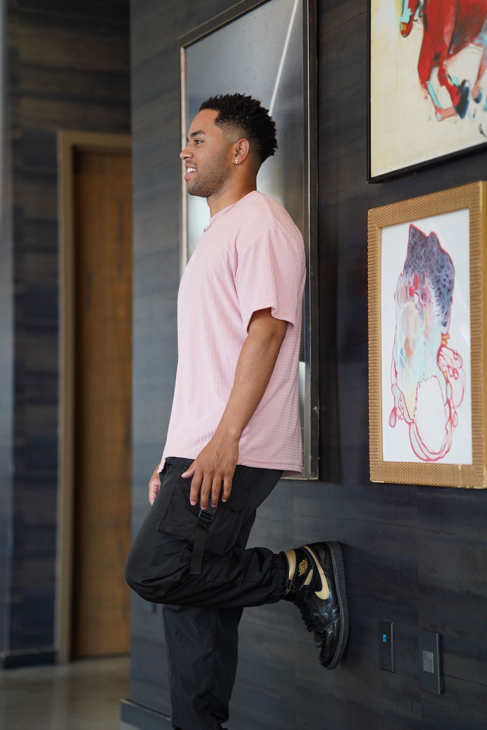 Person in pink shirt and dark pants standing near art gallery wall with framed artwork.