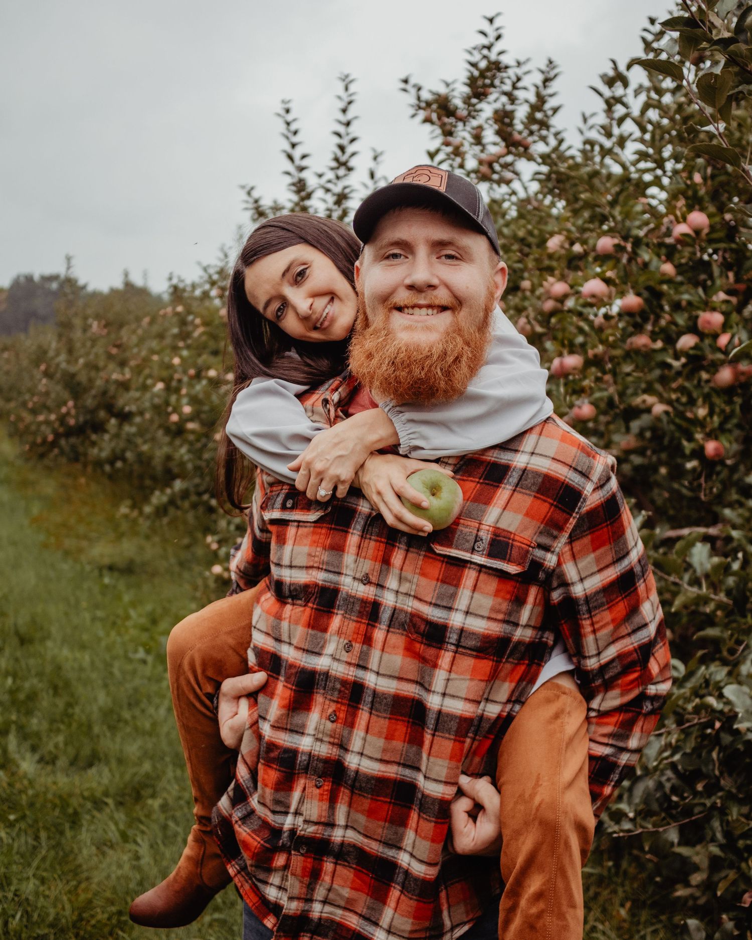 Couple sharing playful moment in apple orchard wearing plaid flannel.