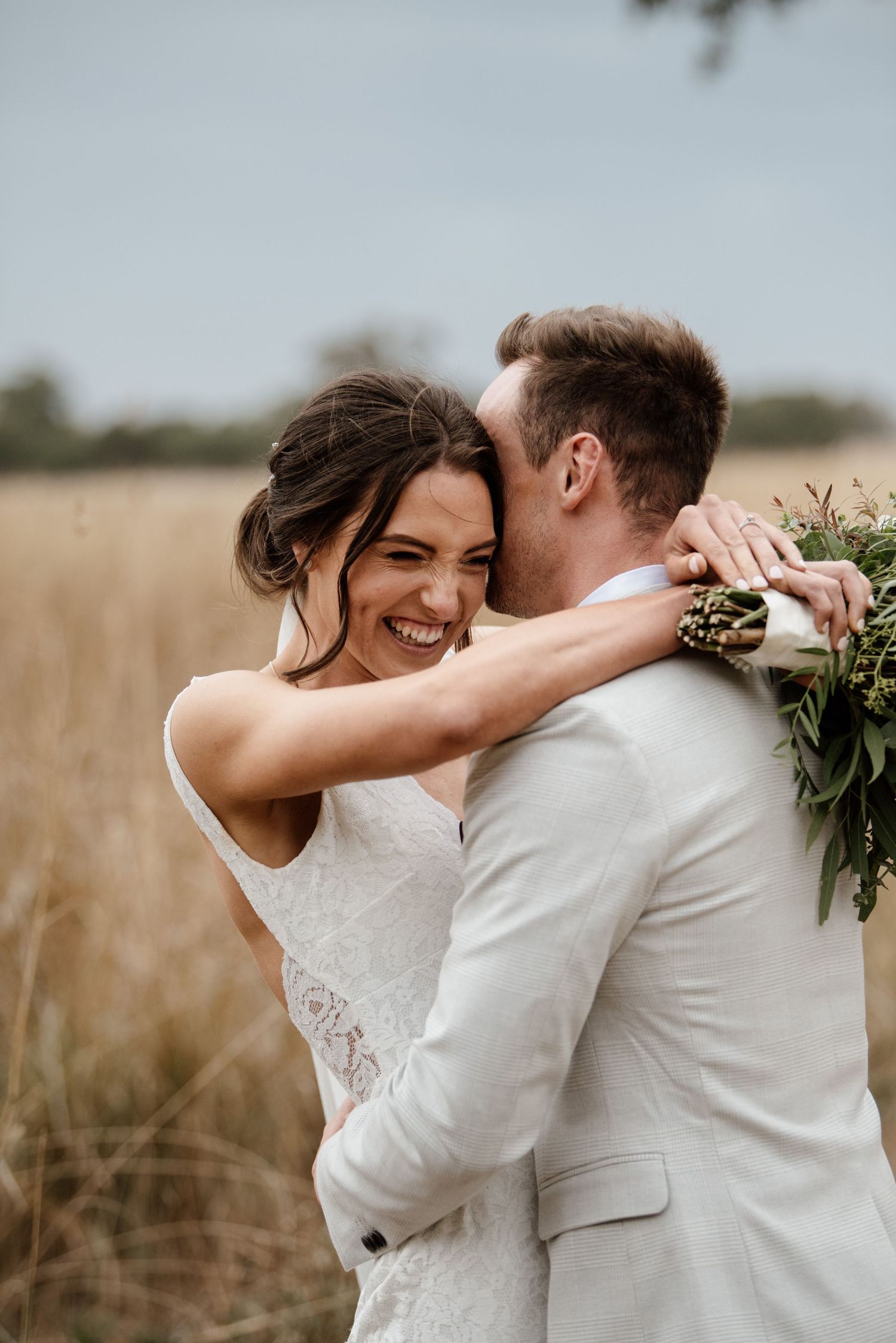 A joyful wedding couple embraces in a golden wheat field during their countryside photoshoot.