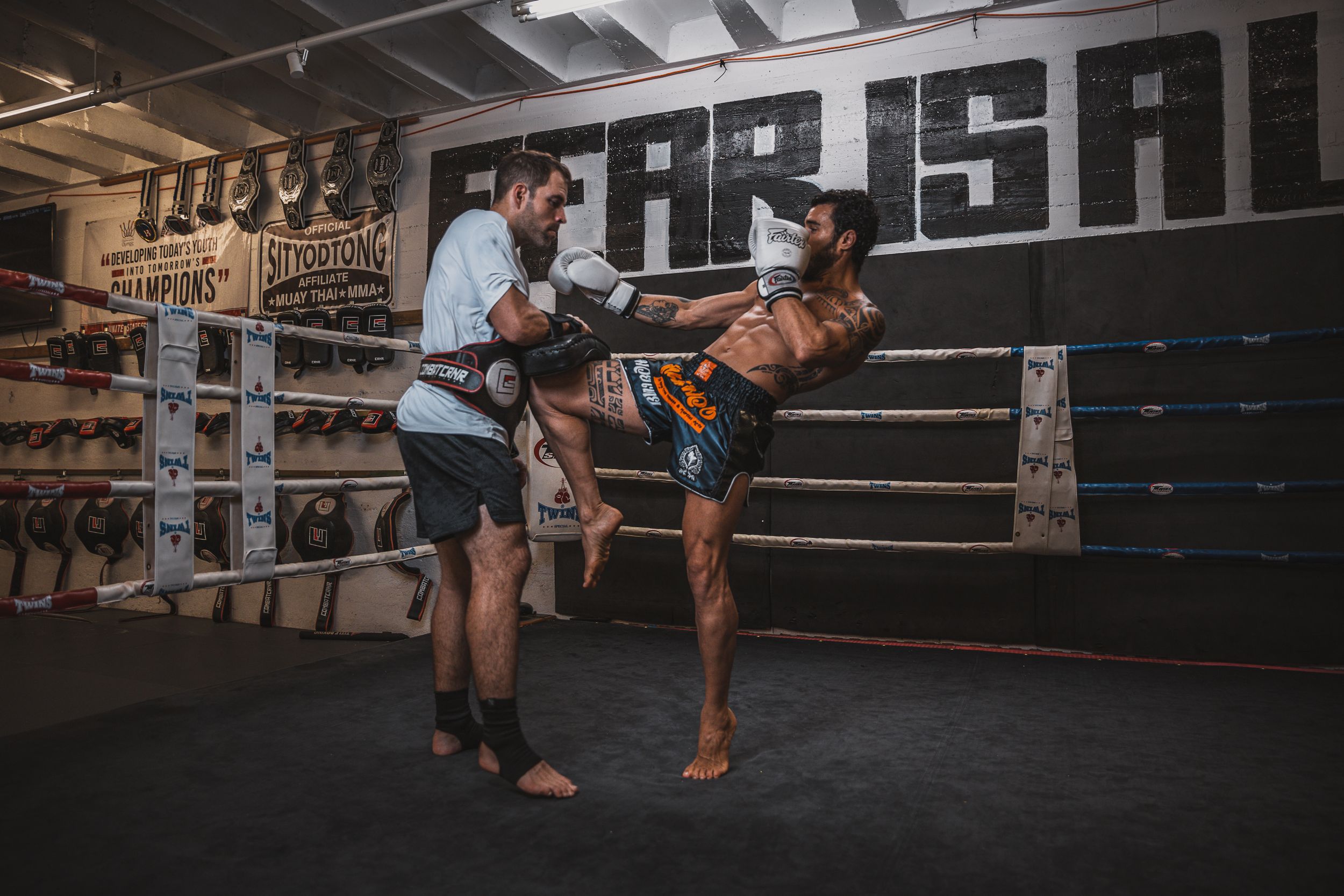 Two fighters practicing Muay Thai kicks and techniques in a boxing gym.