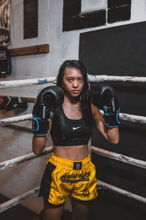 Female fighter in yellow shorts and black sports top training in boxing ring.