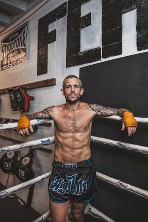 Fighter in blue shorts showing boxing stance against gym wall with equipment.