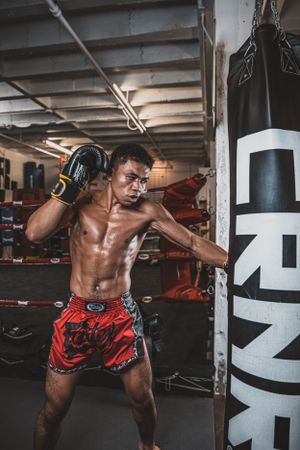 Muay Thai fighter demonstrating high kicks in training gear against black and white backdrop.