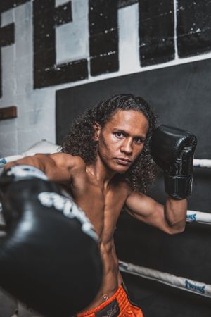 Fighter throwing powerful strikes near boxing equipment in dramatic lighting.