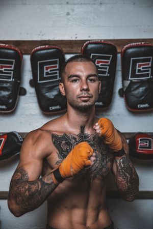 Fighter with detailed tattoos and orange gloves demonstrating boxing stance in gym setting.