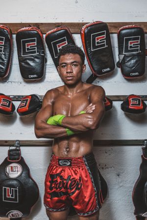 Fighter poses confidently against wall of boxing gloves in training gym.