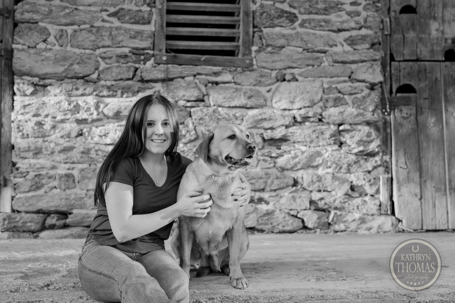 Black and white photo of person and golden retriever dog posing by stone wall.