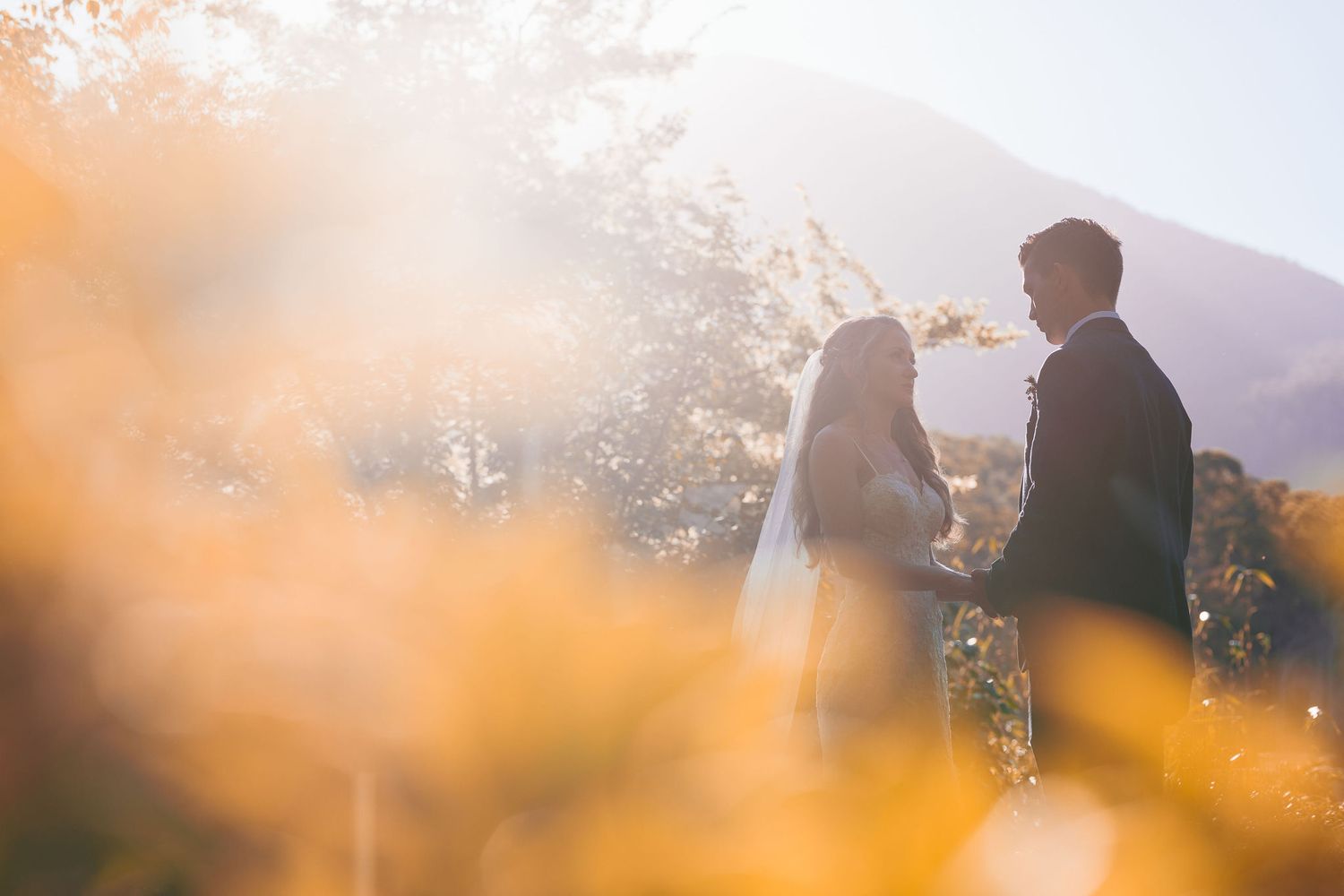 Silhouetted couple stands together against mountain backdrop during sunset.