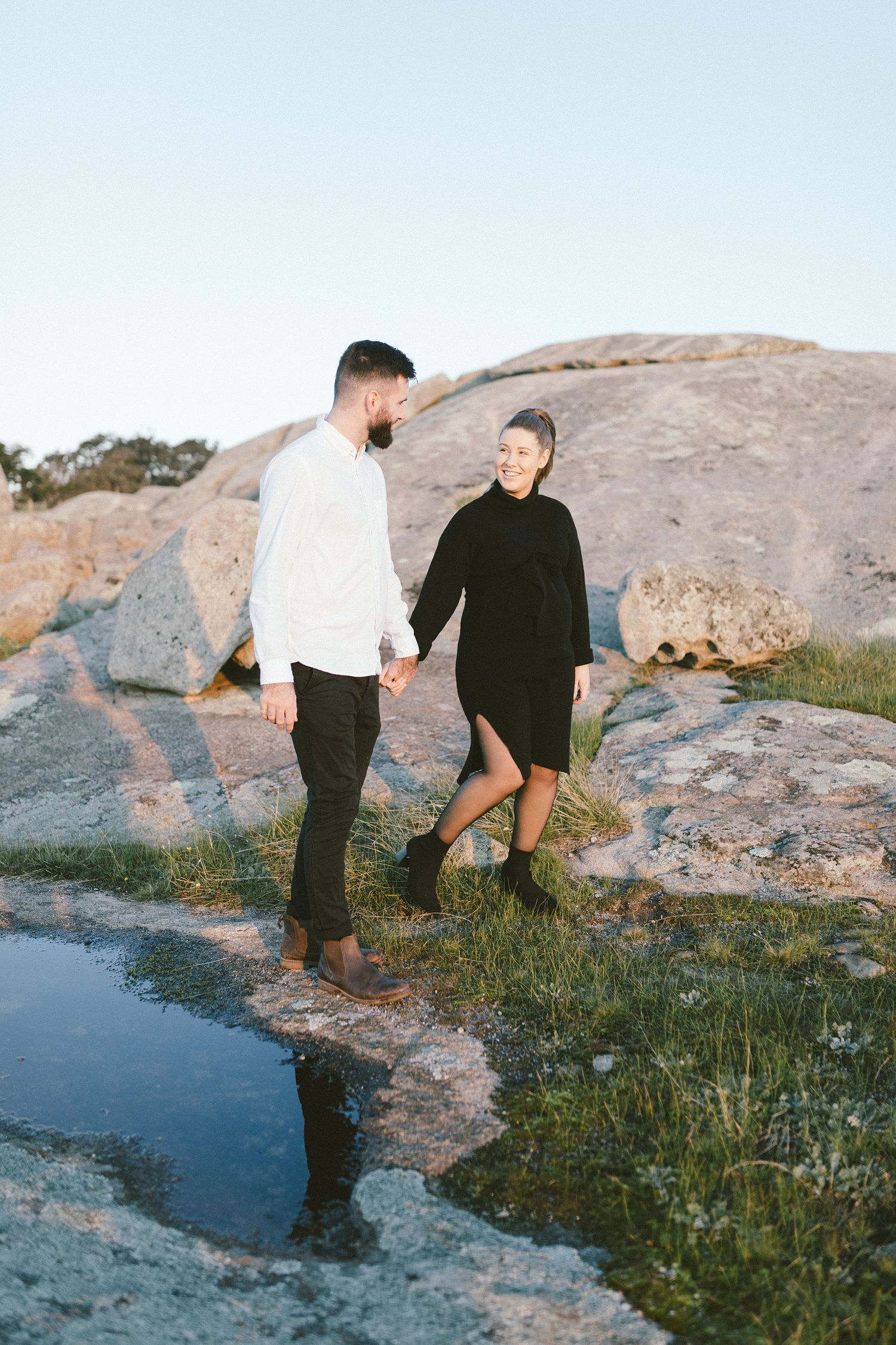 Couple standing by water reflection on rocky terrain.