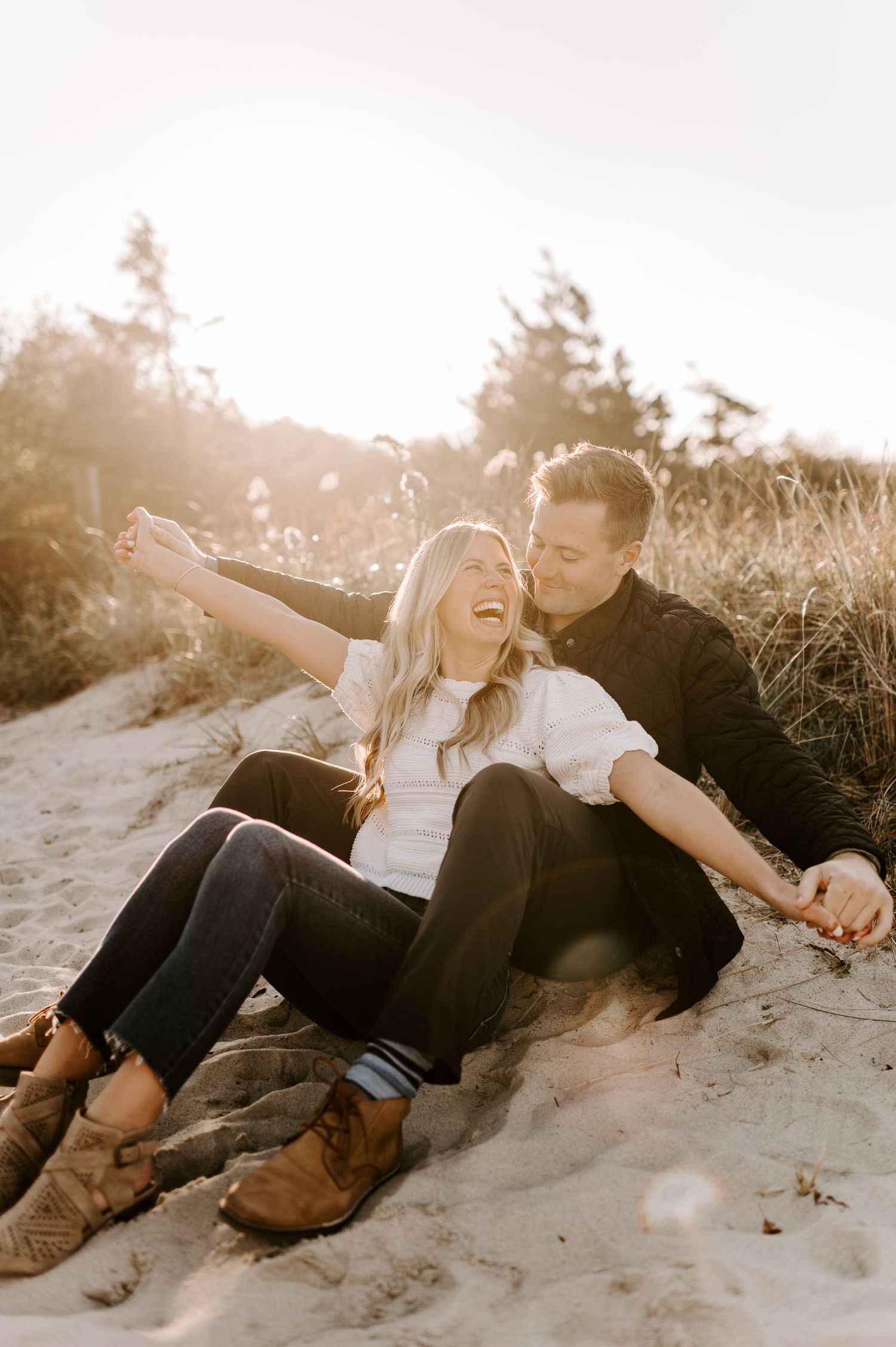 Playful couple relaxing on sand dunes at sunset.