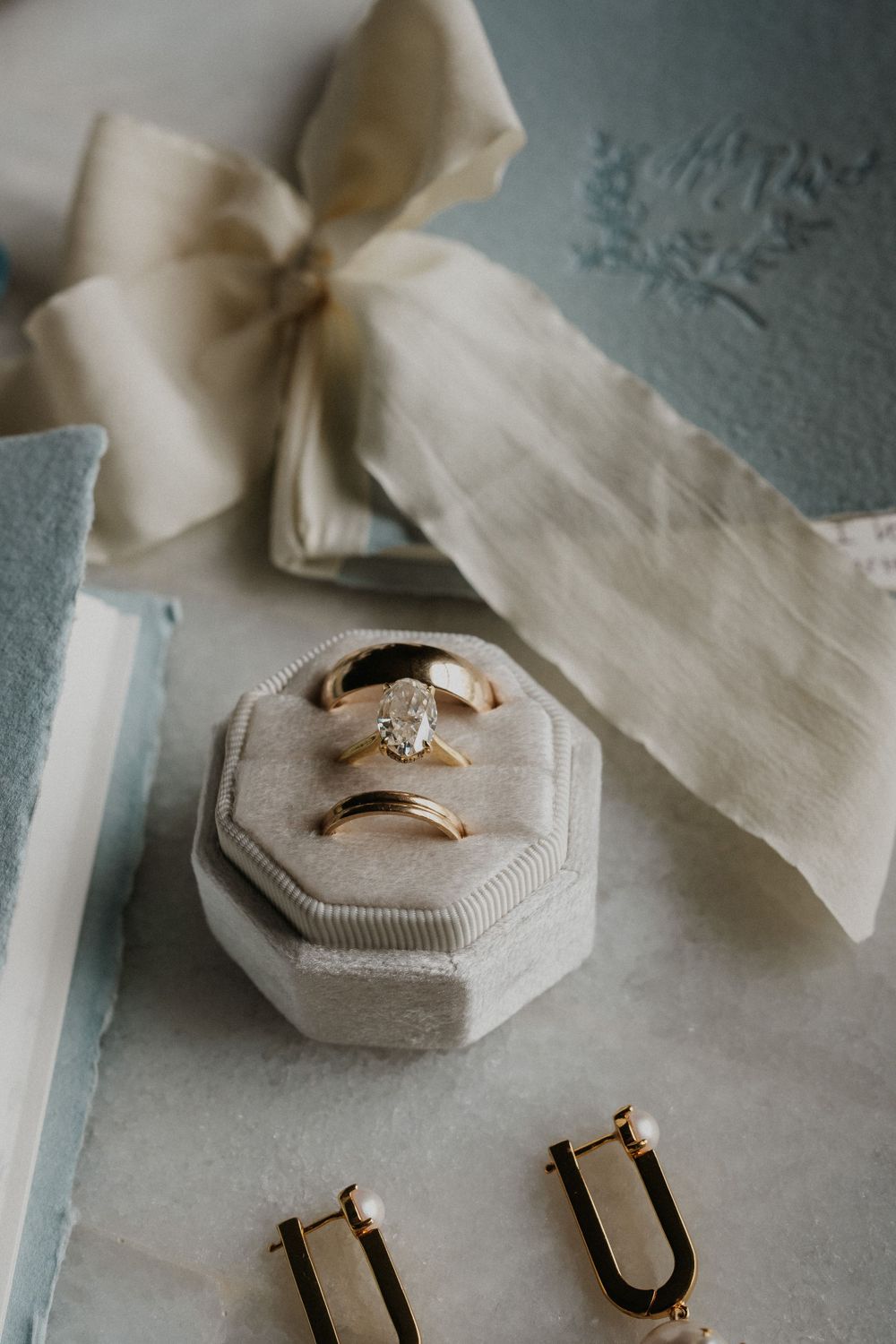 Wedding rings and silk ribbon styled on a textured surface.