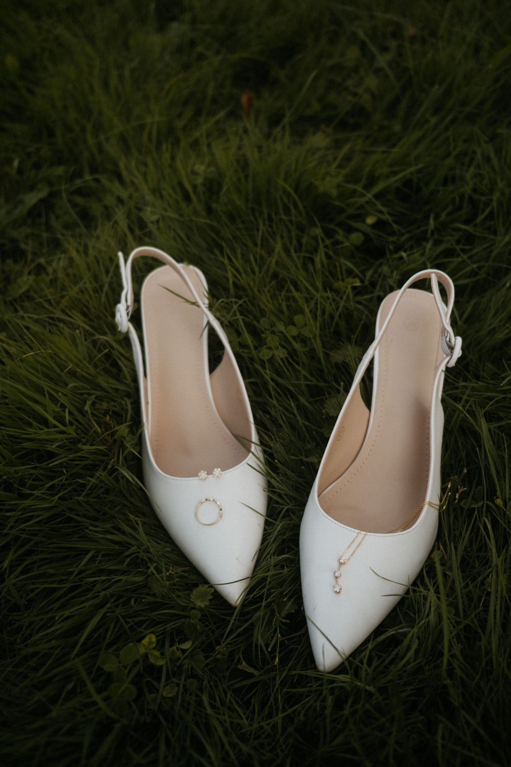 White bridal shoes placed on grass during wedding day photoshoot.