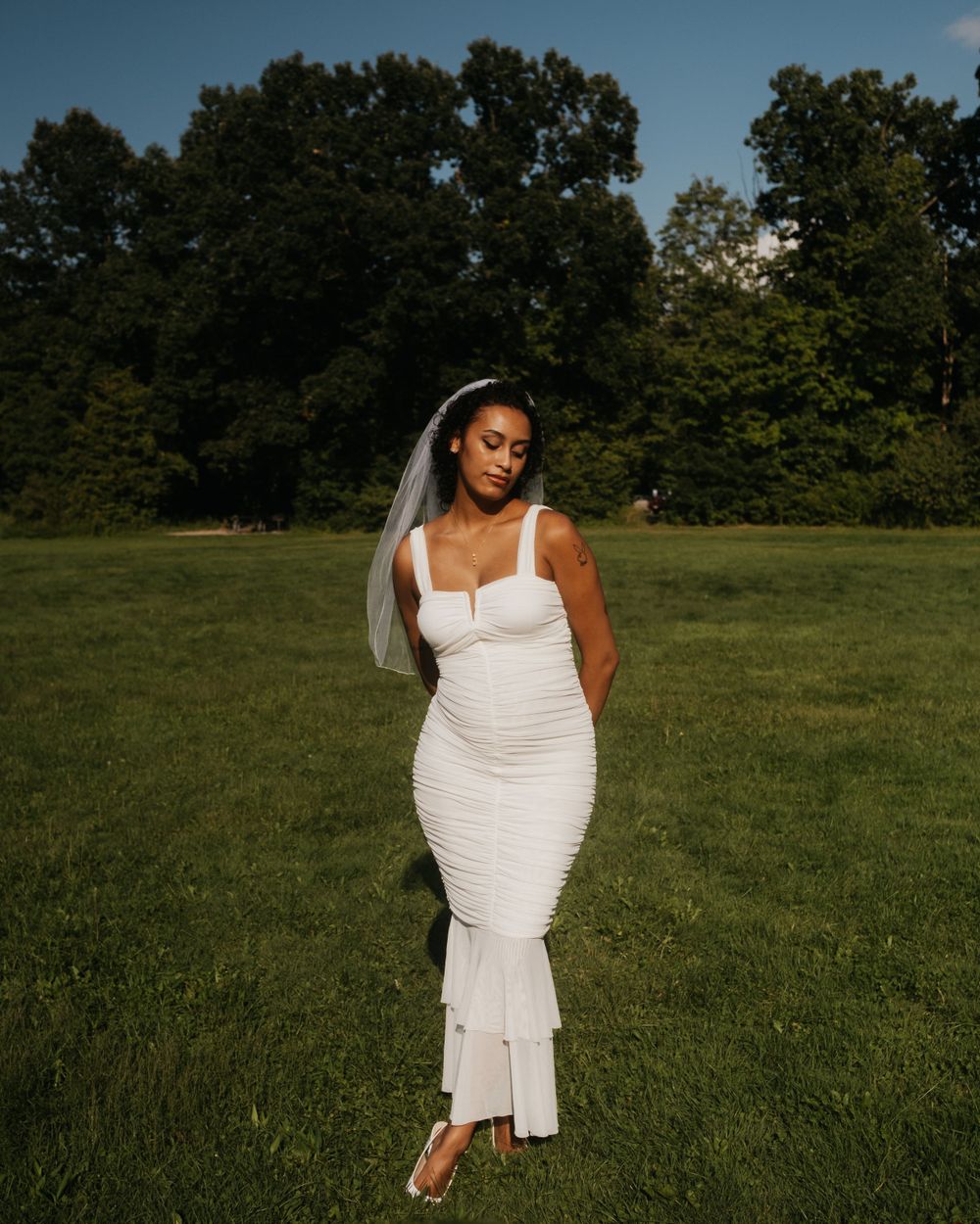 Bride in white dress poses gracefully in a sunny meadow.