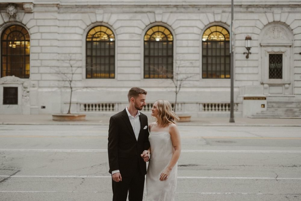 Wedding couple walking together outside historic stone building.
