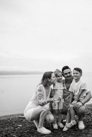 Black and white family portrait on rocky beach with water backdrop.