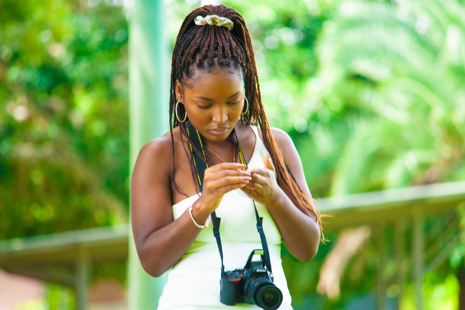 Photographer checking camera settings outdoors with lush greenery in background.
