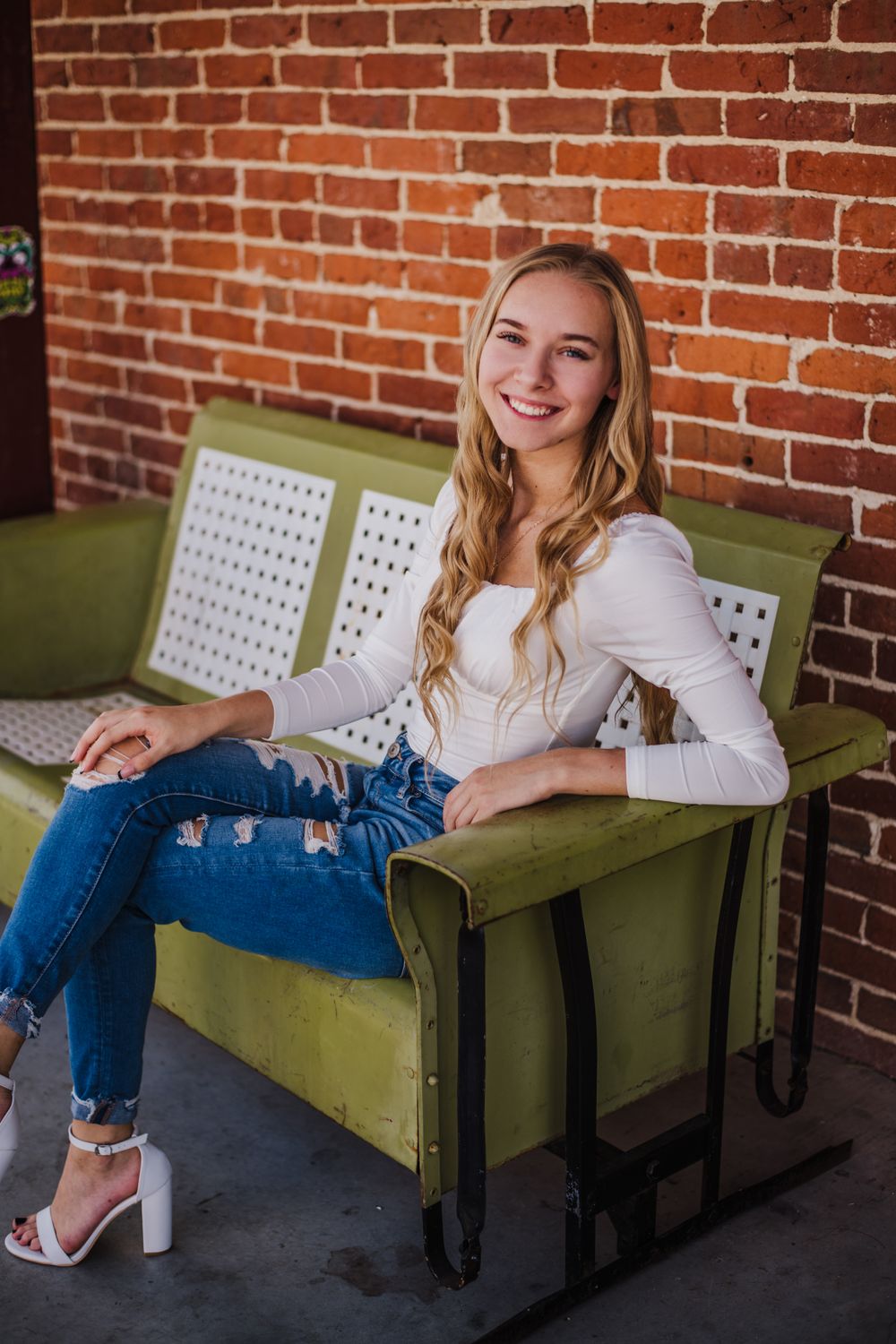 Relaxed pose on vintage green bench against rustic brick wall background.