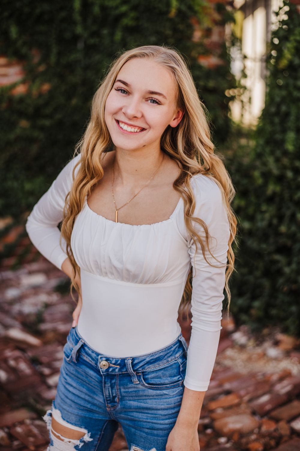 Outdoor portrait with white top and distressed jeans against natural foliage.