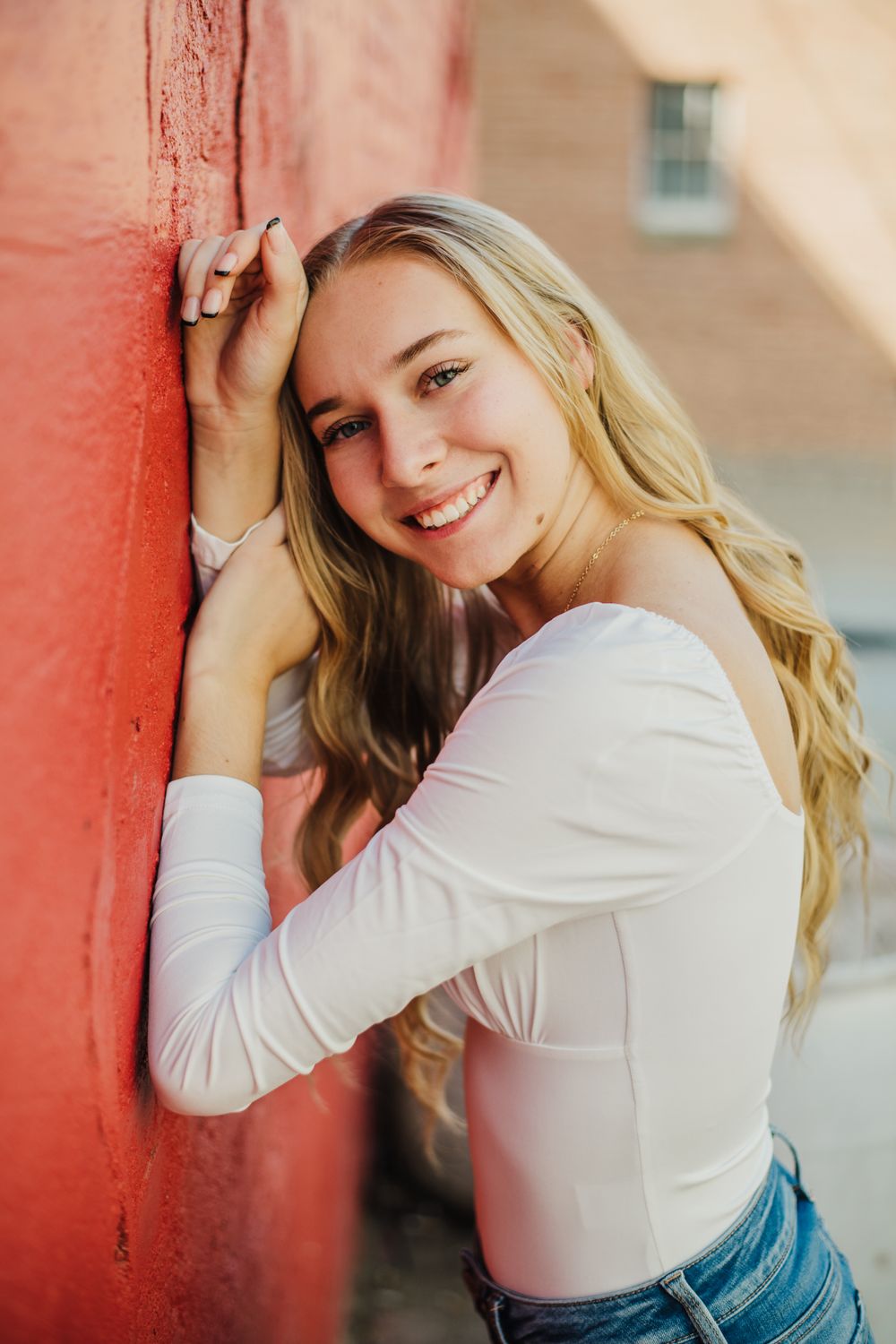 Lifestyle portraits with red brick backdrop featuring white long sleeve top and denim.