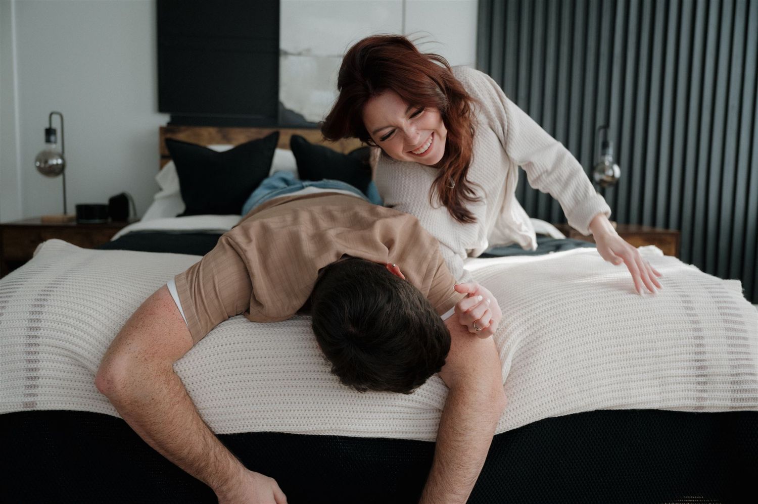 Two people sharing intimate moments while resting on white bedding in a contemporary room.
