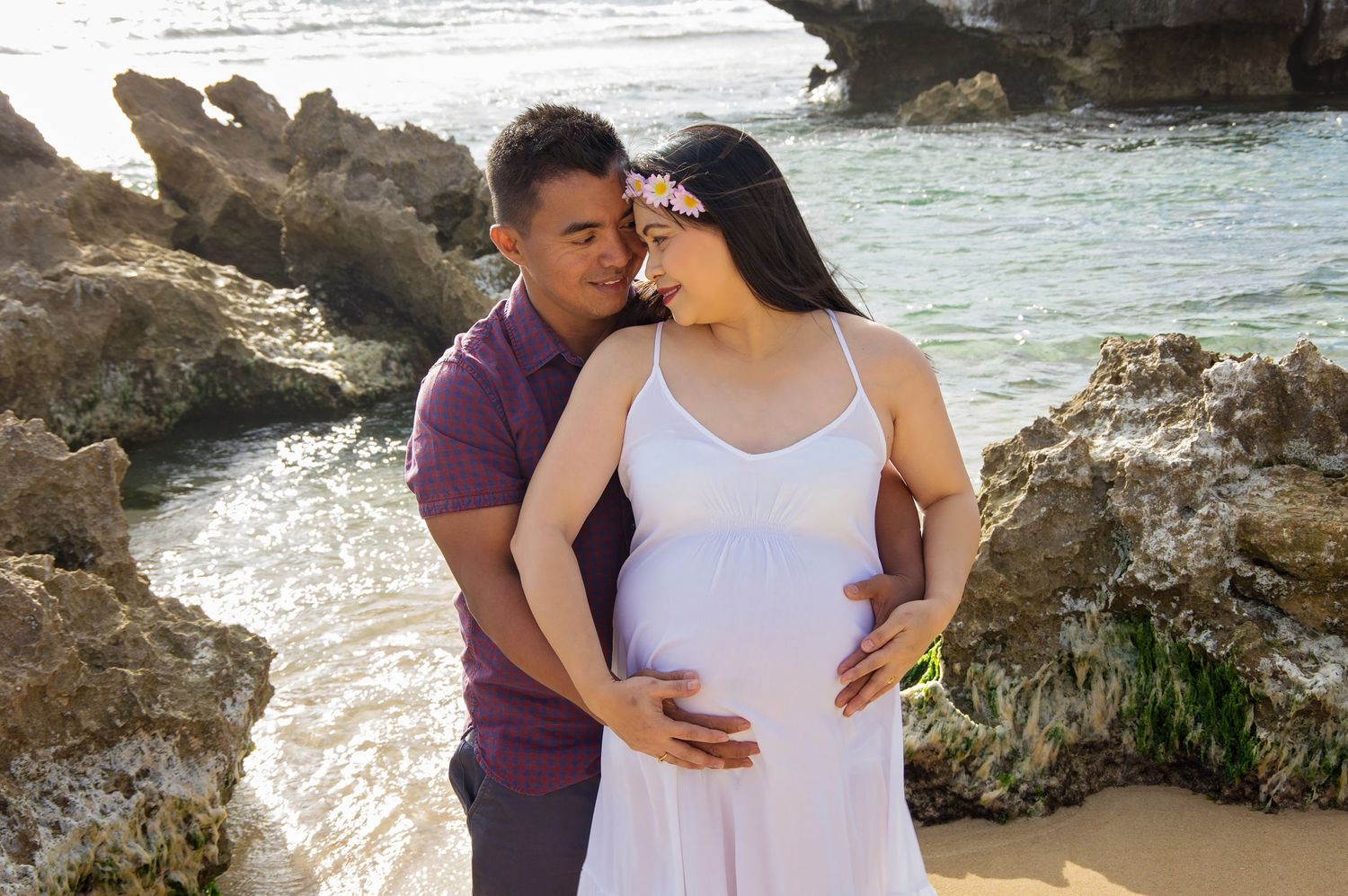 couple embracing pregnant belly on beach