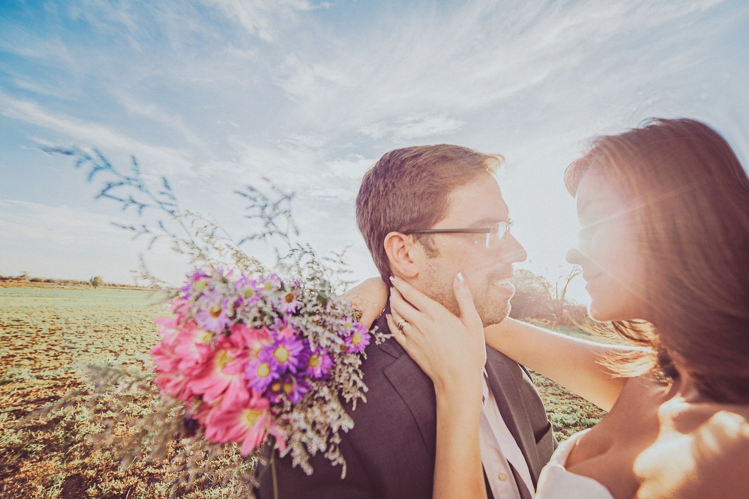 A romantic countryside engagement photo with colorful wildflower bouquet at sunset.