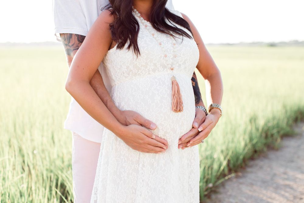 Side view of pregnant woman in white dress standing on marsh pathway.