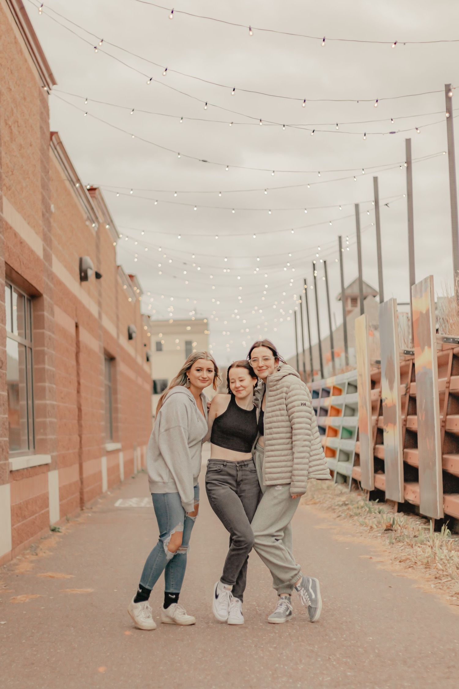 Friends having fun walking and posing together along a brick path with string lights overhead.