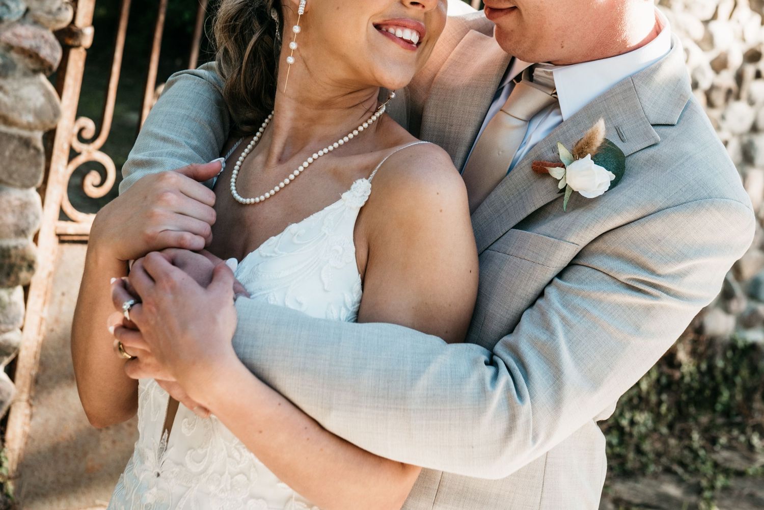 Intimate wedding photo showing tender embrace in formal attire against stone wall.