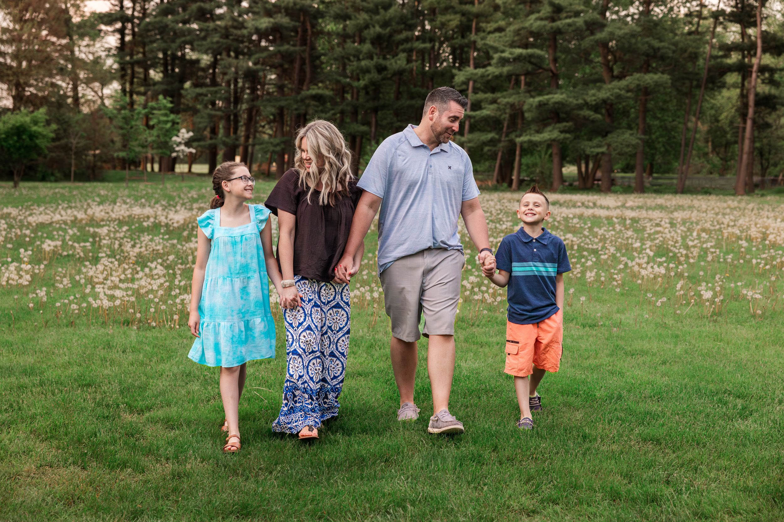 Family taking an afternoon stroll together across an open field with pine trees.