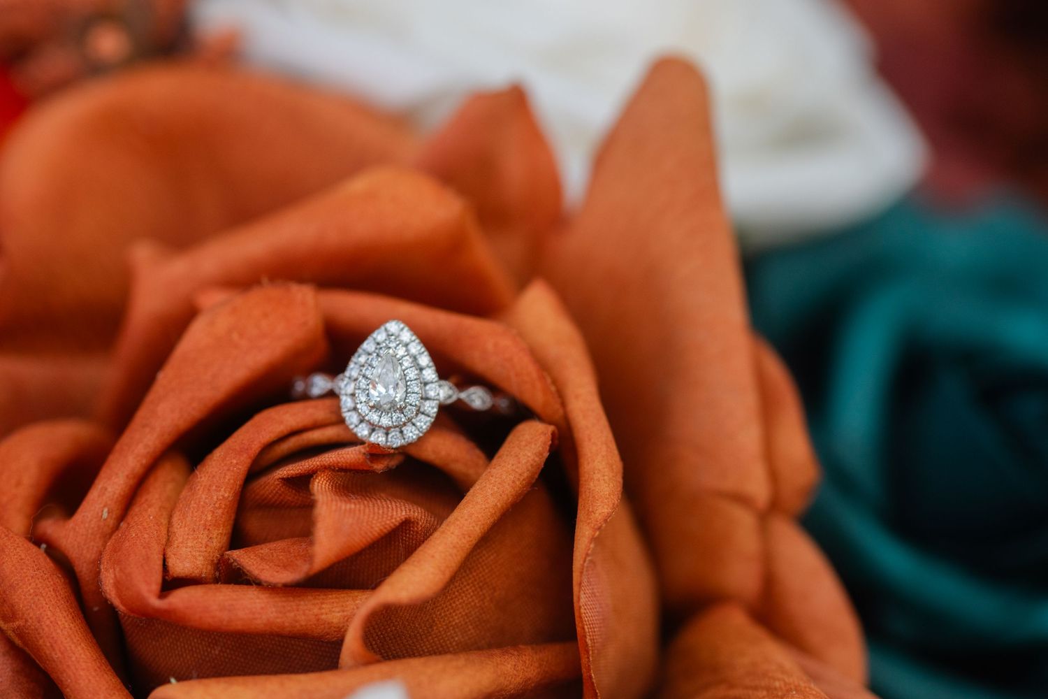 Close-up of burnt orange roses with a sparkling diamond engagement ring.