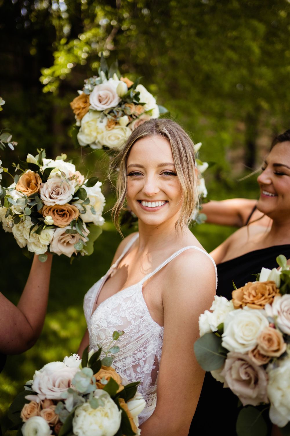 A bridal party poses with peach and white bouquets in a sunny garden setting.
