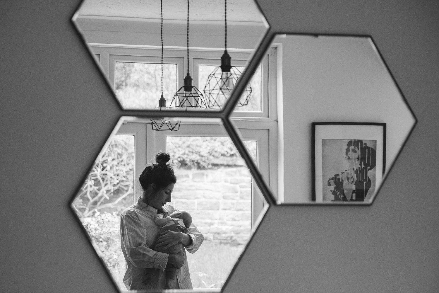 Black and white image of hexagonal mirrors reflecting interior scenes with pendant lights.
