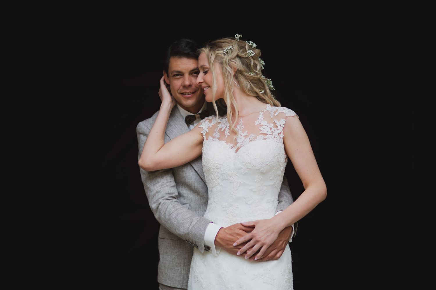 An intimate wedding portrait against a black background showcasing elegant bridal attire.