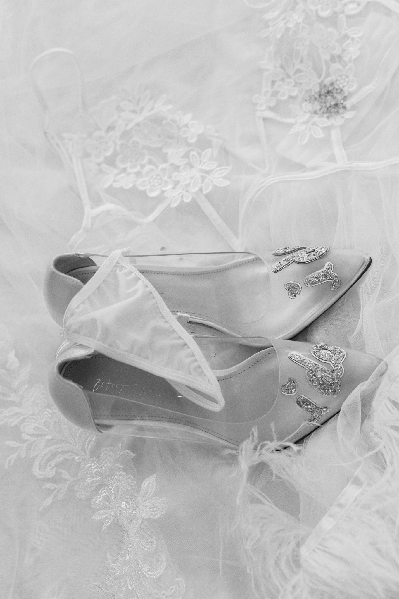 Delicate white wedding shoes with lace and crystal embellishments on tulle fabric.