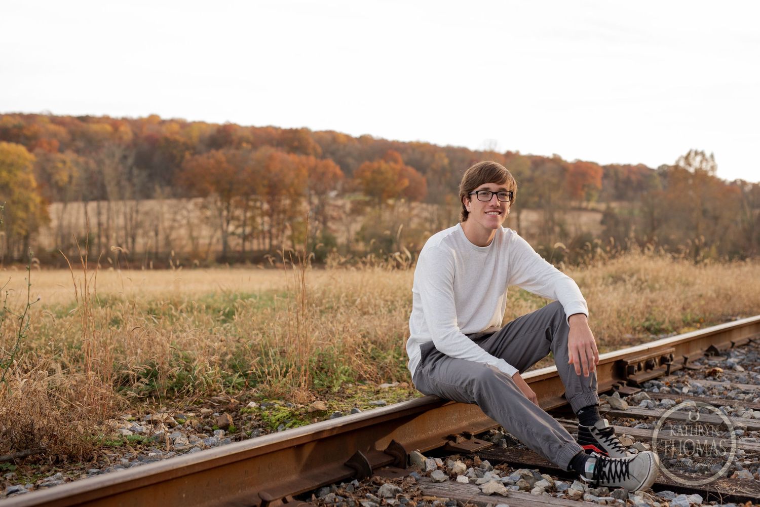 Casual portrait sitting on railroad tracks in autumn landscape.