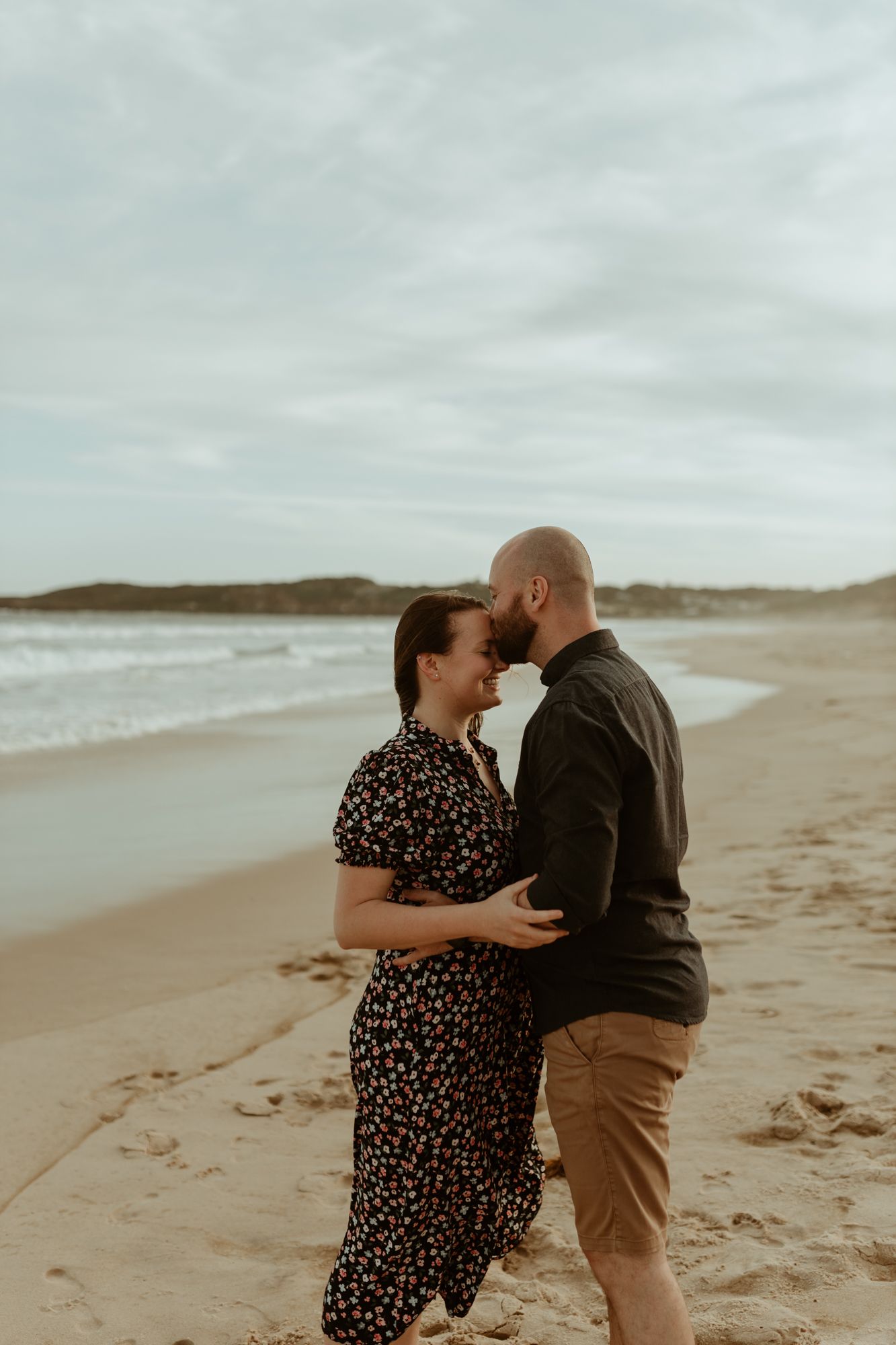 A romantic couple embraces on a secluded beach at dusk.
