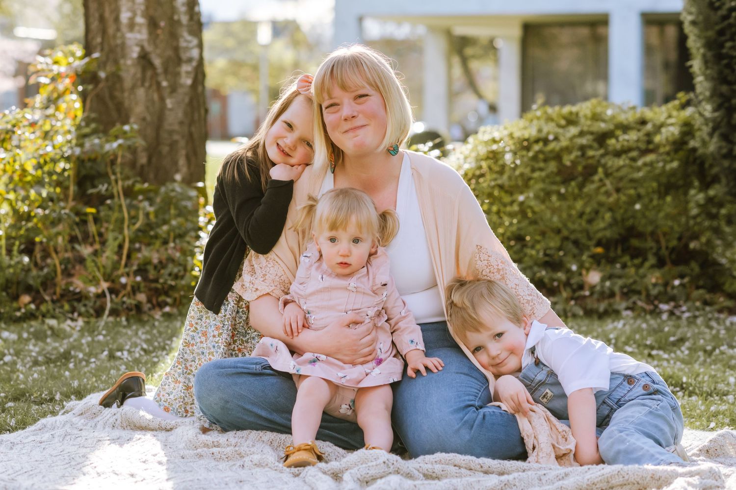 mom and three kid sitting on blanket all smiling and looking at camera.