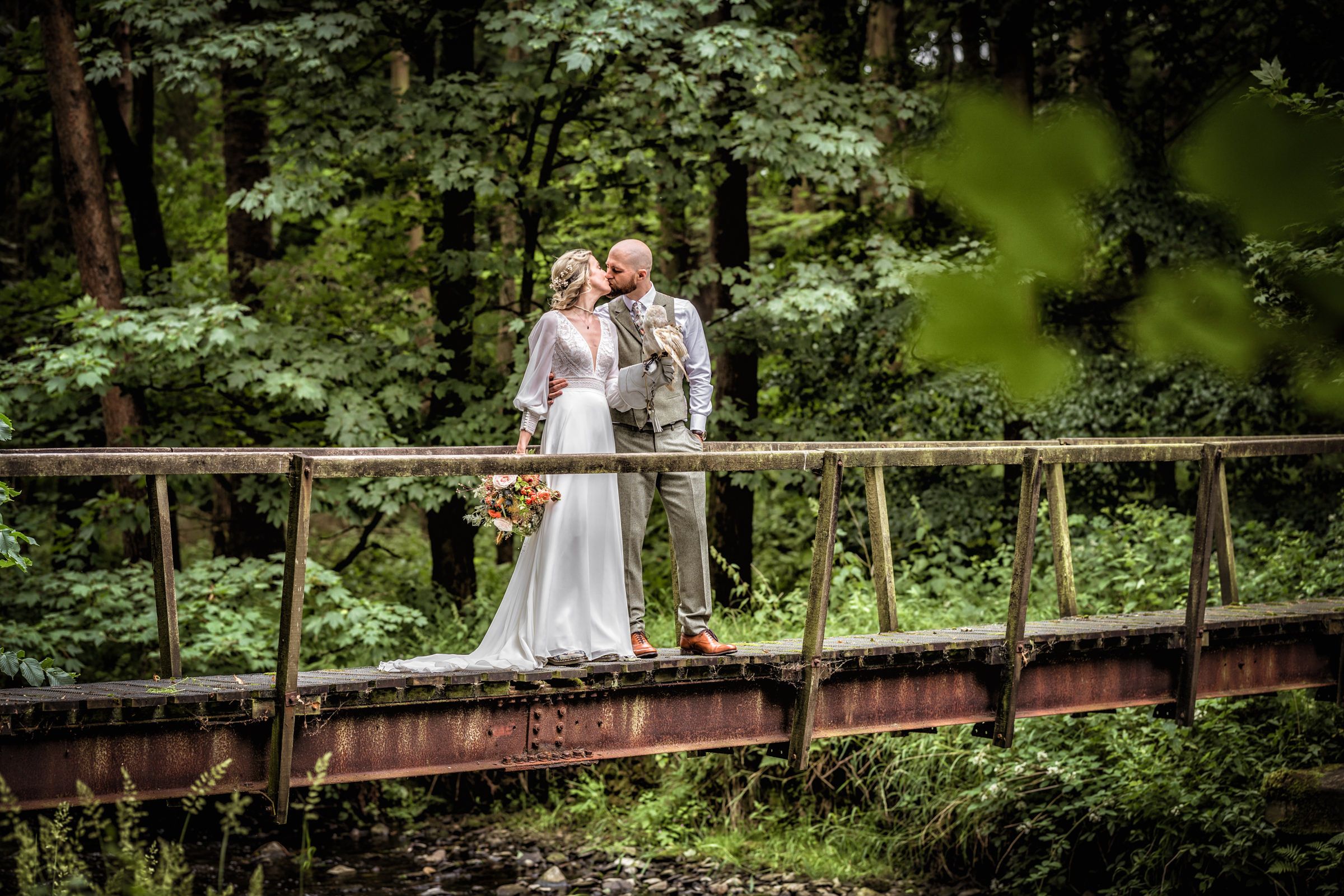 A romantic wedding portrait captured on a rustic wooden bridge surrounded by lush greenery.