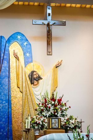 Church altar decorated with religious artwork, crucifix, and floral arrangements.