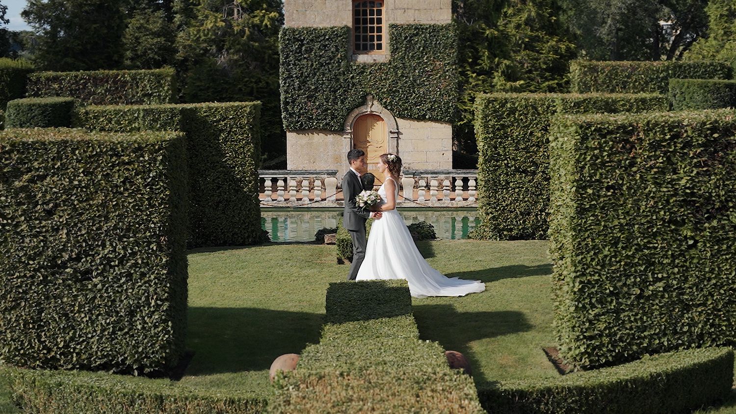 A wedding couple poses together in a formal garden with perfectly trimmed hedges and pathways.