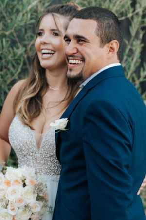 Joyful wedding portrait with couple sharing laughter against garden greenery.