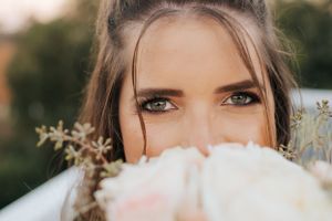 Close-up portrait of bride peeking over her white rose bouquet.