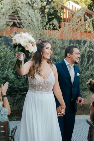 Celebratory moment with newlyweds walking down aisle holding white rose bouquet.