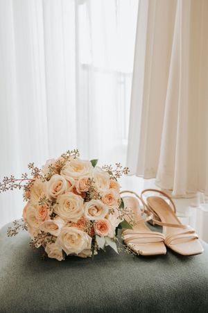 Blush pink rose bridal bouquet with nude heels on grey velvet surface.