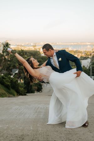 Wedding couple performs romantic dip pose on scenic overlook during sunset photoshoot.