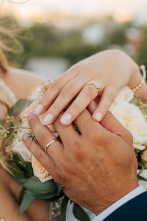 Close-up of newlyweds' hands with wedding rings and white rose bouquet details.