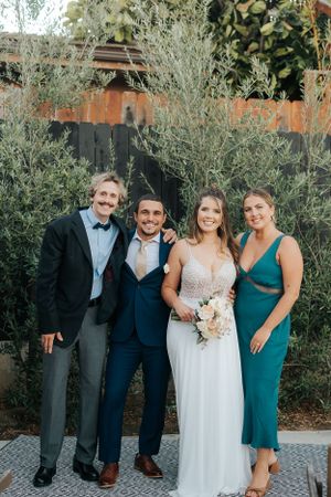 Wedding party of four people pose together in front of garden greenery.