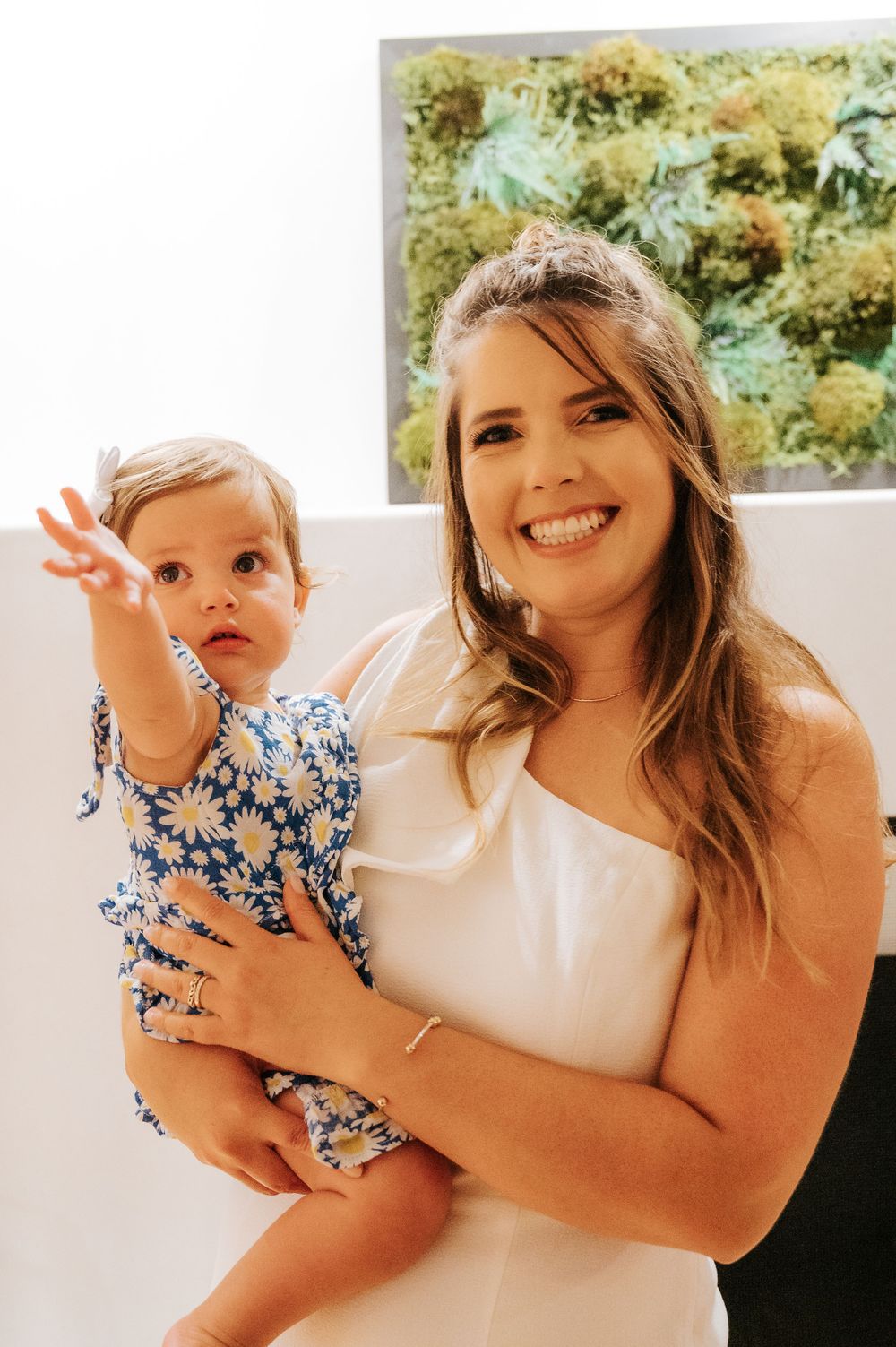 Mother and daughter share playful moments in white dresses against bright background.