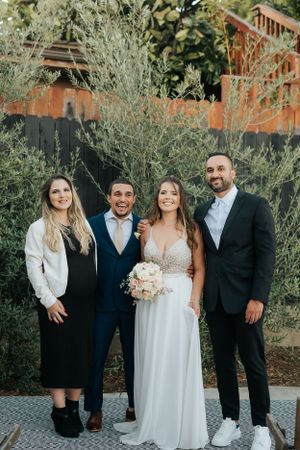 Wedding party poses outdoors against wooden wall with greenery backdrop.